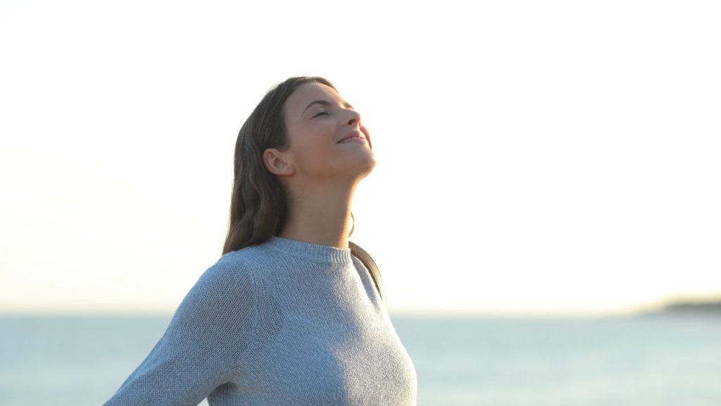 Woman at the beach with her arms flung out as she takes a deep breath of oxygen.